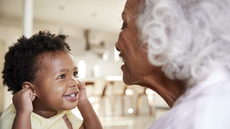 Grandmother and grand baby face to face smiling. By Monkey Business Images. Article on when a mother wants grandkids and pressures her daughter