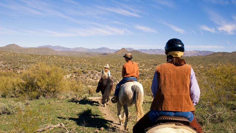people horseback riding in the desert, image by Danny Raustadt. While there are countless ways to explore the world, few can match the heart-pumping rush and soul-enriching experience of horseback vacations.
