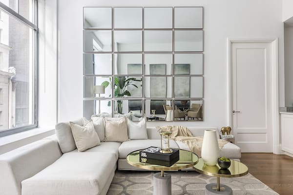 Living room with mirror walls. Select glass as opposed to wood for surfaces. Glass and transparency automatically add a sense of airiness to a space. Mirrors can help to make ceilings feel taller and higher, part of a use of space-saving tips.