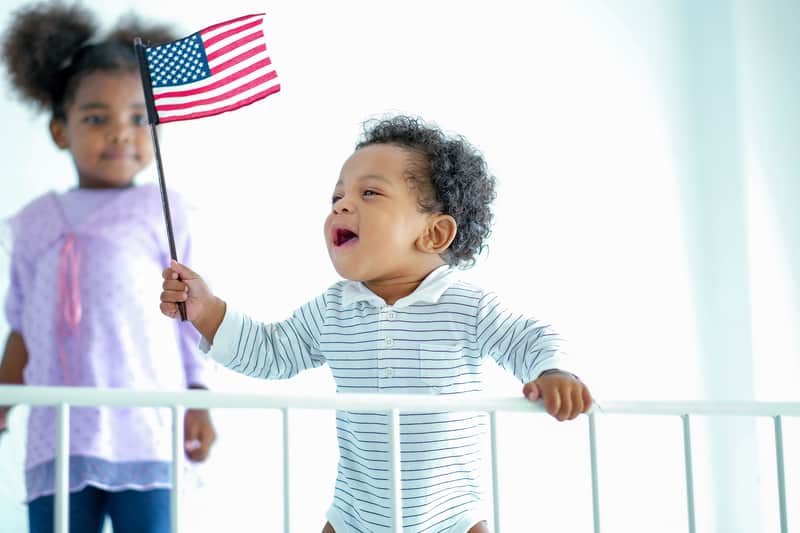 adorable African American baby with flag, with his sister in the background. Image by Narongrit Sritana