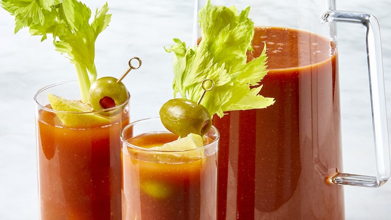 Two individual glasses of Bloody Mary, with olive and celery for garnish, and a pitcher of Bloody Mary. How to make a Bloody Mary from scratch and tailor it to your tastes.