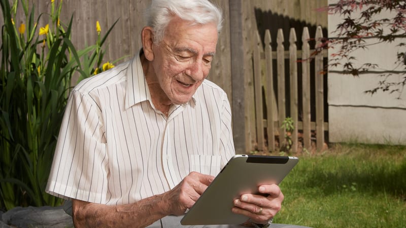 an older man outside using a tablet, possibly doing a puzzle like Boggle and go birding, or reading