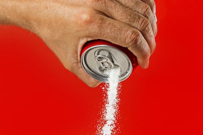 A man's hand pouring out soda, but pure sugar is coming out. By Ocusfocus. Article on how and why to quit drinking soda.