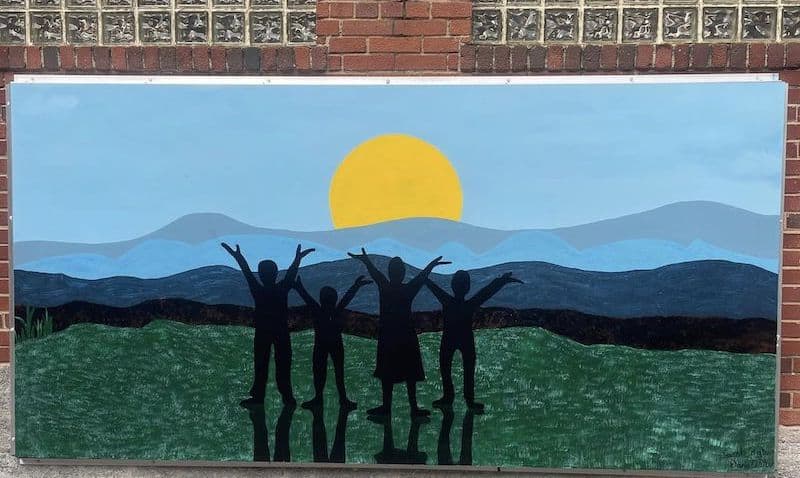 Mural of children reaching to the sky, in front of the sunset over the Blue Ridge Mountains, in Grandin Village near Roanoke, Virginia. Image by Kari Smith