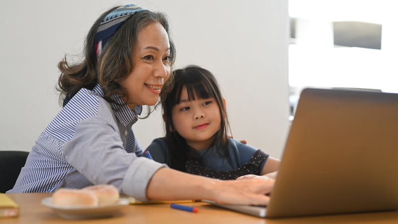 grandmom and granddaughter on a laptop, possibly doing puzzles and games. Prathan Chorruangsak