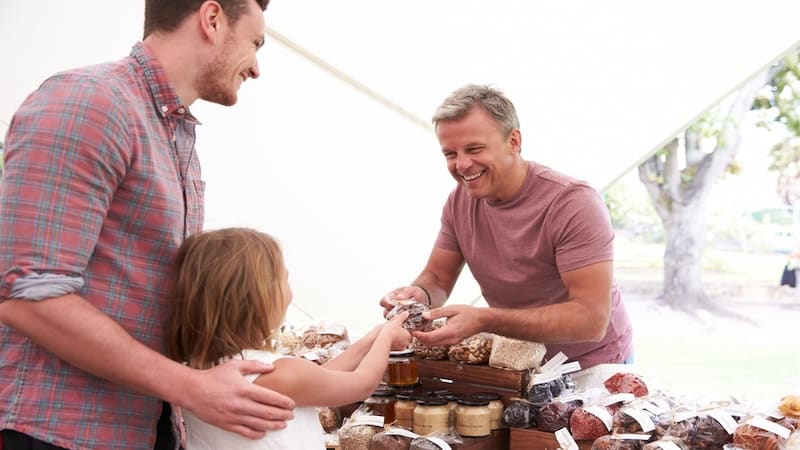 A little girl and her father buying from a vendor at a farmers market. Image by Monkey Business Images