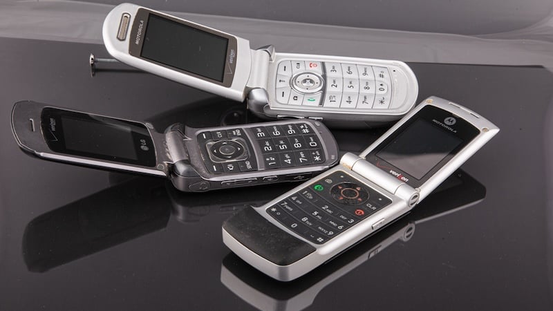 three old cell phones on a black background, for article on Flip Phone February. Image by Darryl Brooks