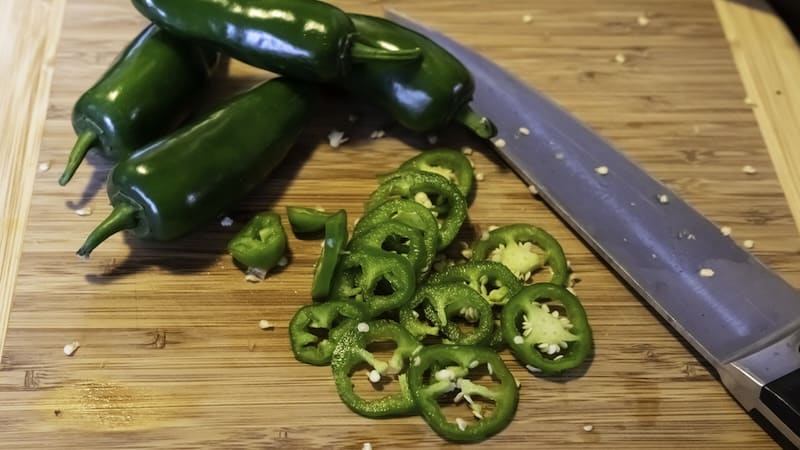 a knife with whole and sliced jalapeño peppers on a cutting board. Image by Jacqueline Nix. Article on healing jalapeño hands