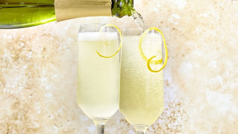 Topping off two French 75 cocktails with Champagne from a bottle. This classic cocktail is a mix of gin, lemon juice, and simple syrup, with Champagne poured on top.