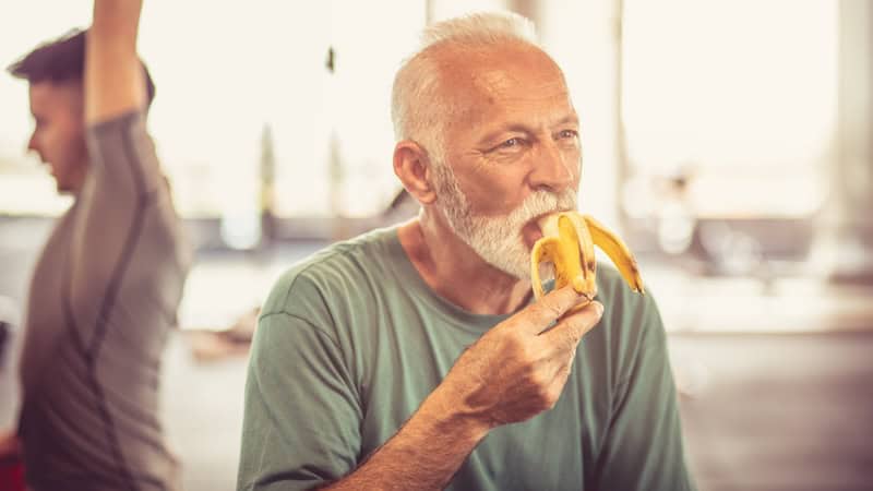 Knowing he should eat before a workout, a man is eating a banana in a gym. Image by Malden Zivkovic