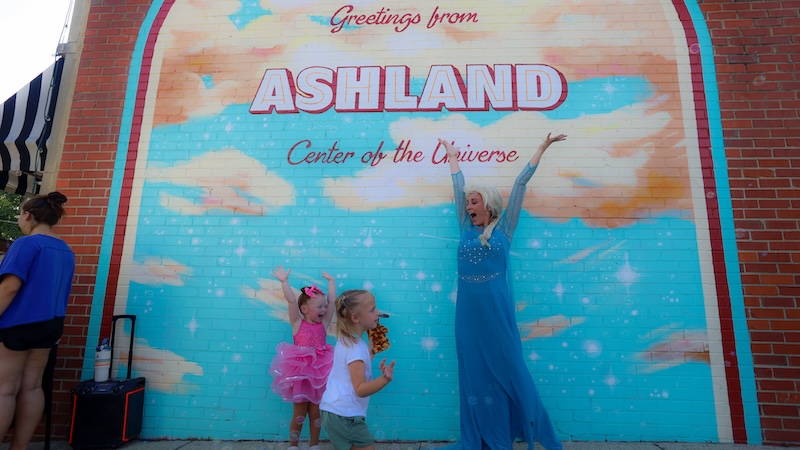 A woman and two girls in front of a mural in Ashland, Virginia, Provided by Downtown Ashland Association. Used in What's Booming: Rhythm and Resilience