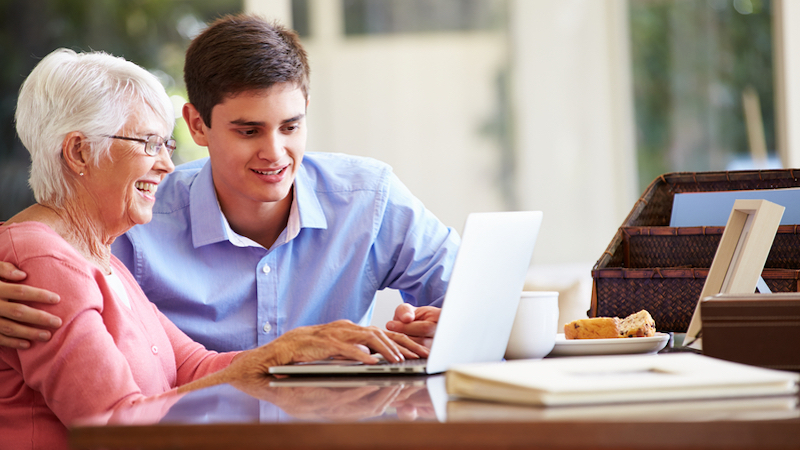 Grandmother with young adult grandson at a computer, possibly doing a puzzle or game like the Find the Furniture Boggle BrainBuster. By Monkey Business Images.