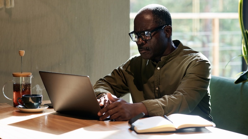 Man doing his online finances, such as making 401(k) contributions. Image by Anna Tolipova