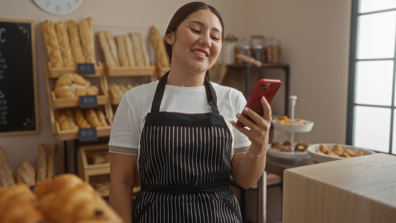 Young woman working at a bake shop, holding a cell phone. Surrounded by young people who are often clueless to the way things used to work, humorist Greg Schwem has learned a few tricks on how to mess with Gen Zers. Image by Aaron Amat