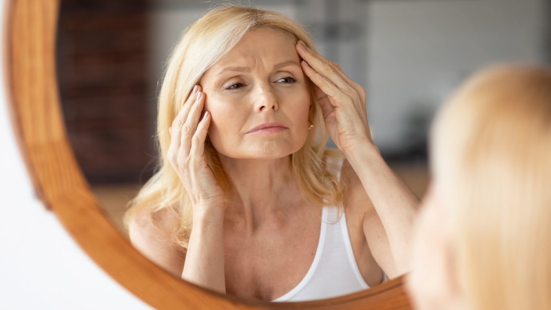 A middle-aged woman looks at herself in the mirror, concerned about aging and wondering, does collagen aid in fighting wrinkles? Image by Prostockstudio