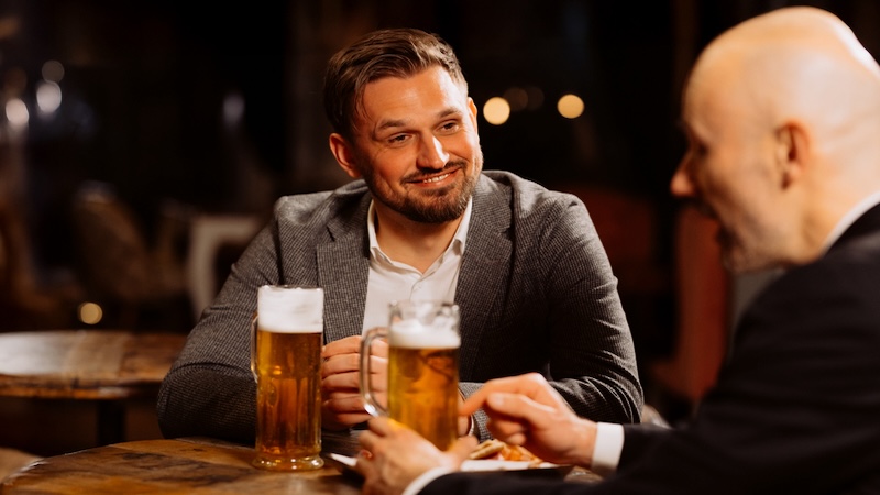 Two men engaged in a bar conversation with beers and bar food. Image by Volodymyr Harasymiv