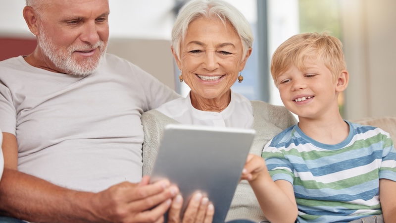 Grandparents and grandson looking at a tablet and smiling, as if doing the humorous kids' Jumble puzzles with runners