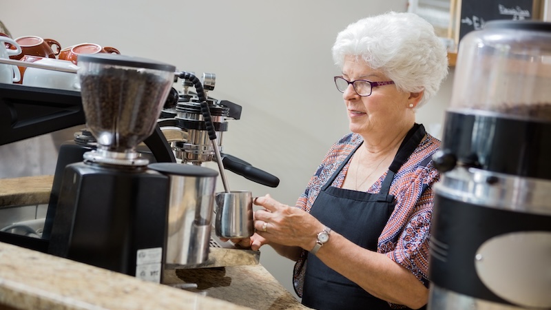 Senior woman working as a barista. 7 Surprising Reasons Retirees Are Going Back to Work. Image and article from Kiplinger Financial