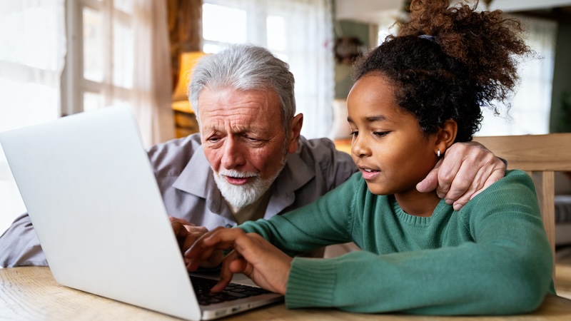 Granddad and granddaughter on a laptop, possibly doing puzzles. By Nd3000