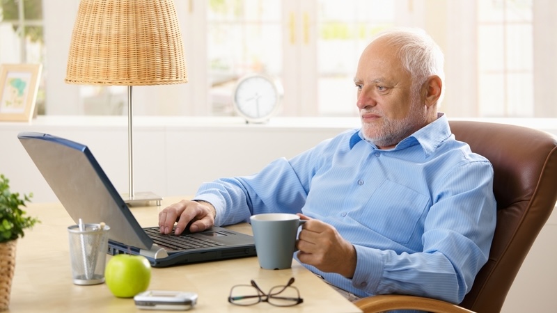 Senior man with a cup of coffee at home, on his laptop. Used with Boggle puzzle