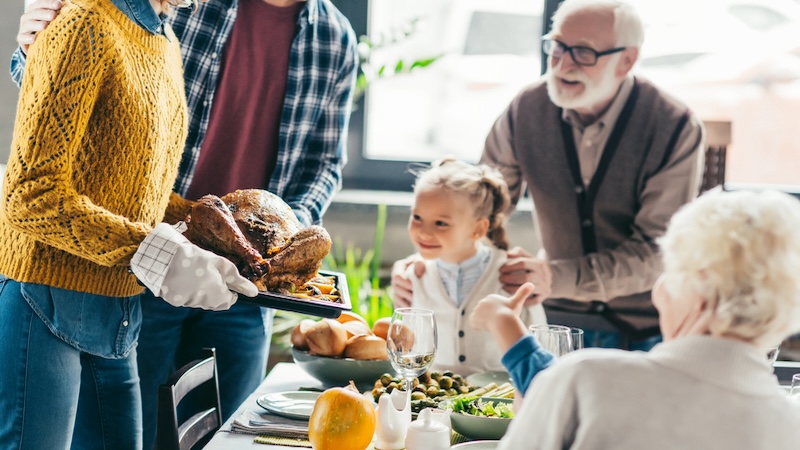 A woman brings a turkey to the Thanksgiving table. The man's bushy nose hair spoils the dinner for some.