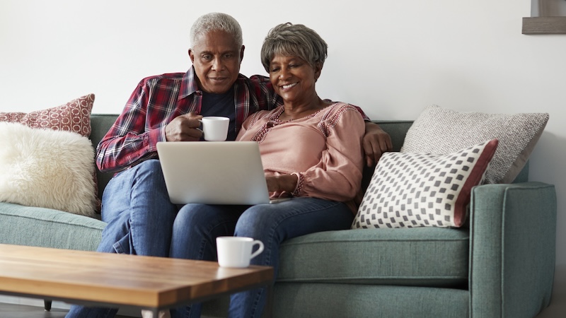 A couple on their sofa looking at a computer, perhaps playing the palindrome Boggle puzzle or other puzzle. Image by Monkey Business Images