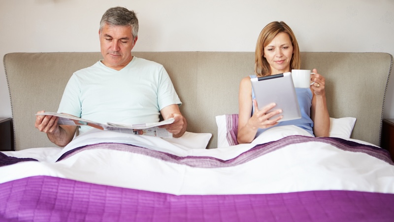 Couple reading in bed, though his bedtime fidgeting can be annoying. By Monkey Business Images