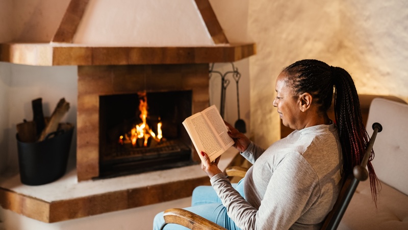a woman relaxing with a book in front of a cabin fireplace as part of a microvacation. By Alessandro Biascioli