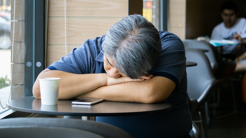 Tired man at a public table. If you are sleepy during the day, it may be a sign that you aren't getting enough sleep at night, furthering the risk of the sleep and dementia connection. Image: Natthapon M