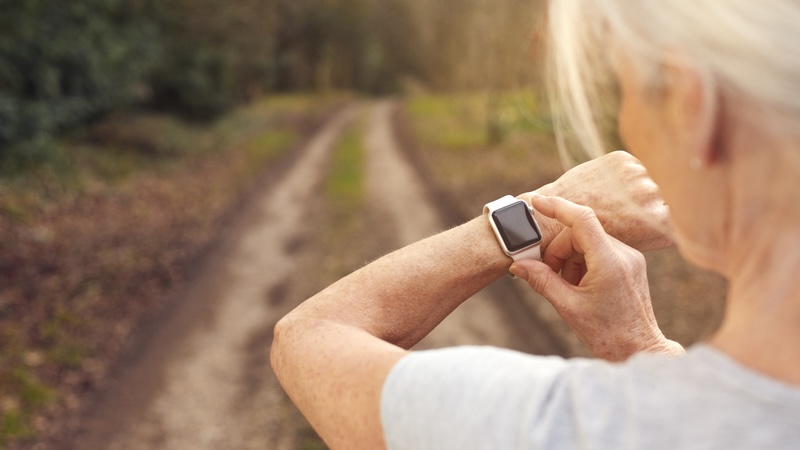 Woman using her smart watch to check her health stats as she walks, knowing why it's important to know your heart rate numbers. By Monkey Business Images