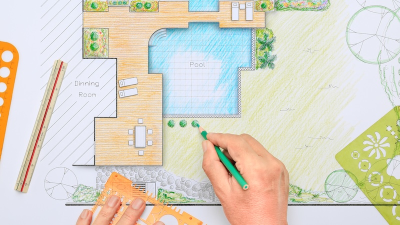 A person drafting a design for a new in-ground pool: In planning a home enhancement, consider the hidden costs of home upgrades