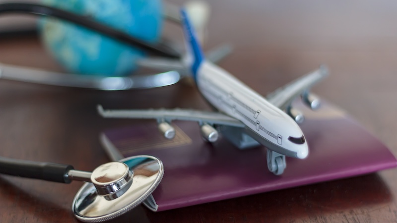A small model airplane, passport cover, globe, and stethoscope: a concept of travel health insurance
