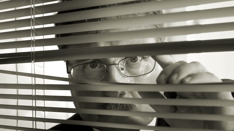 Suspicious man peeking through Venetian blinds. Is that a bad person he sees? Image by Suzanne Tucker