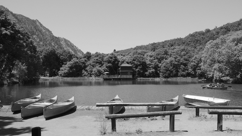 canoes sit empty at the edge of a lake surrounded by mountains, representing camp awakenings for kids. Benjamin Hallam