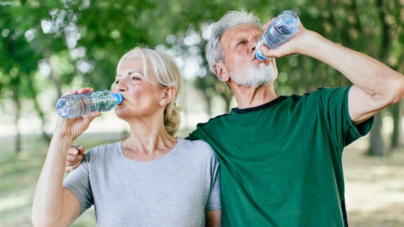 Smiling active senior couple holding water bottles, drinking and jogging together in the park. Why Hydration Matters More Than You Think