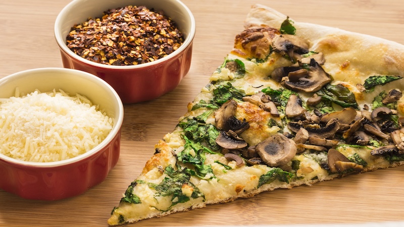 A slice of a healthier pizza with spinach, mushrooms, and a moderate amount of cheese.