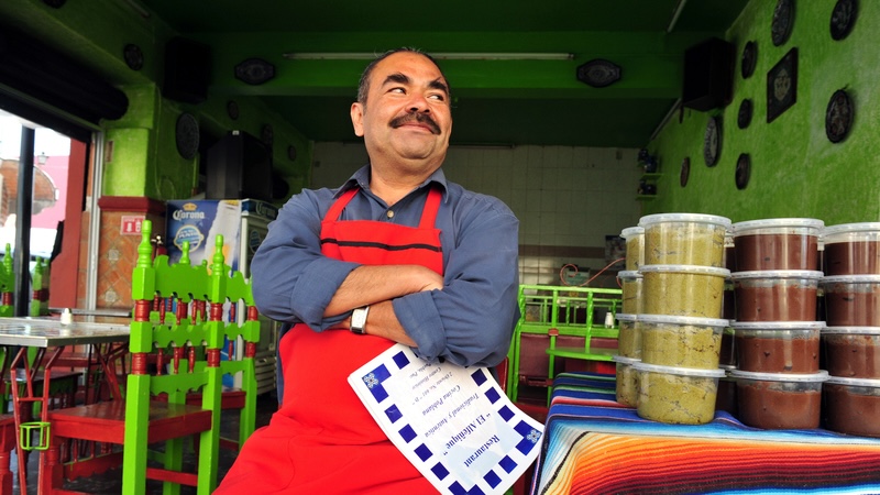 A Mexican entrepreneur in his sit-down restaurant, also selling packaged salsas. On immigrants and Social Security. Rafael Ben Ari