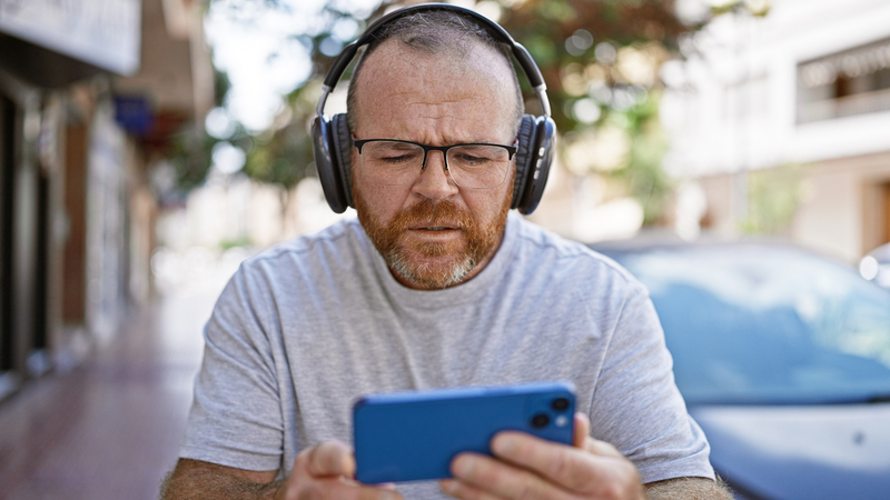A man wearing headphones looking at his smartphone, perhaps listening to Amazon Music. Aaron Amat