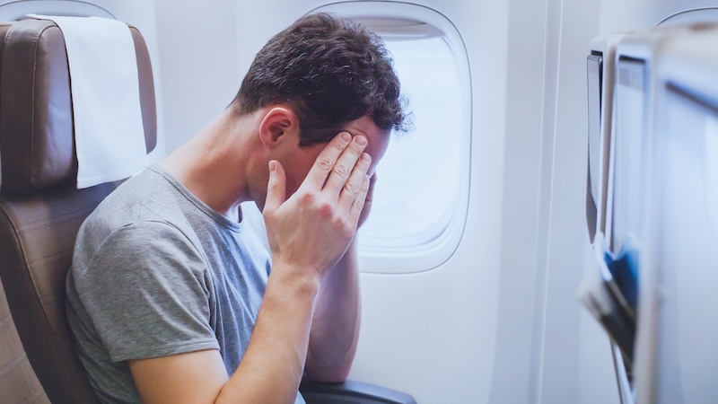 A man holds his head on a plane, needing remedies for motion sickness. Options include special wristbands, funny-looking glasses, and a new drug to curb vomiting. (Dreamstime/TCA)
