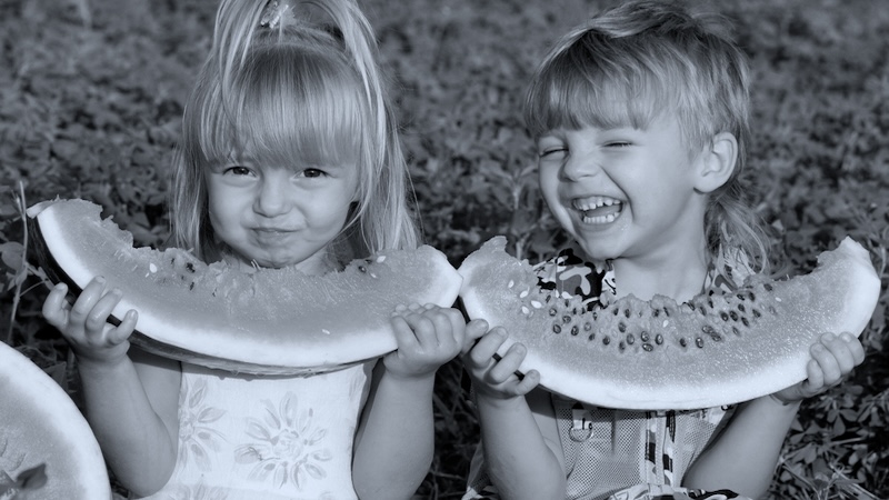Two young female cousins gleefully eating watermelon slices, of family reunions and food. Denys Prokofyev